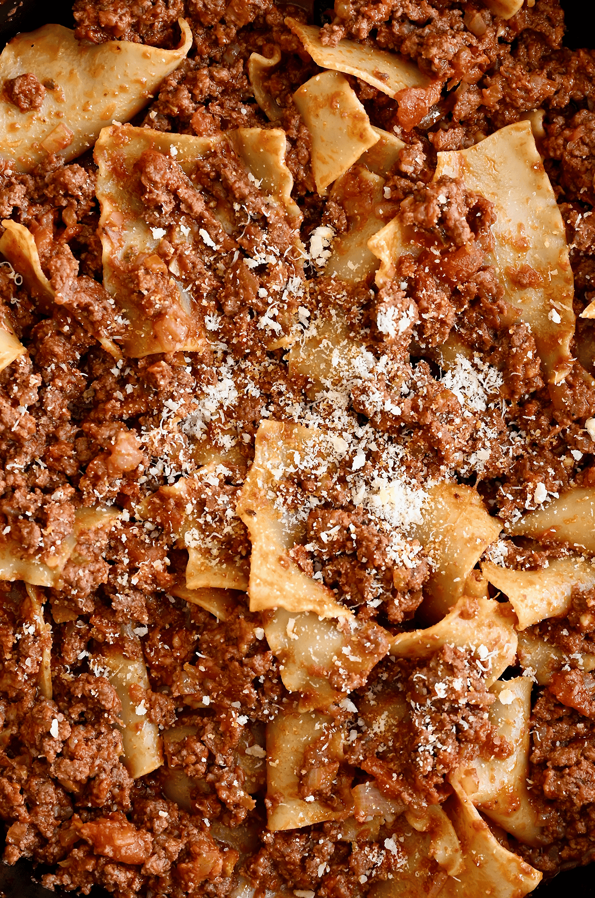 Pieces of lasagna noodles coated in beef marinara sauce and garnished with grated Parmesan cheese.