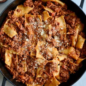 A cast iron skillet containing hearty beef lasagna garnished with grated Parmesan cheese.