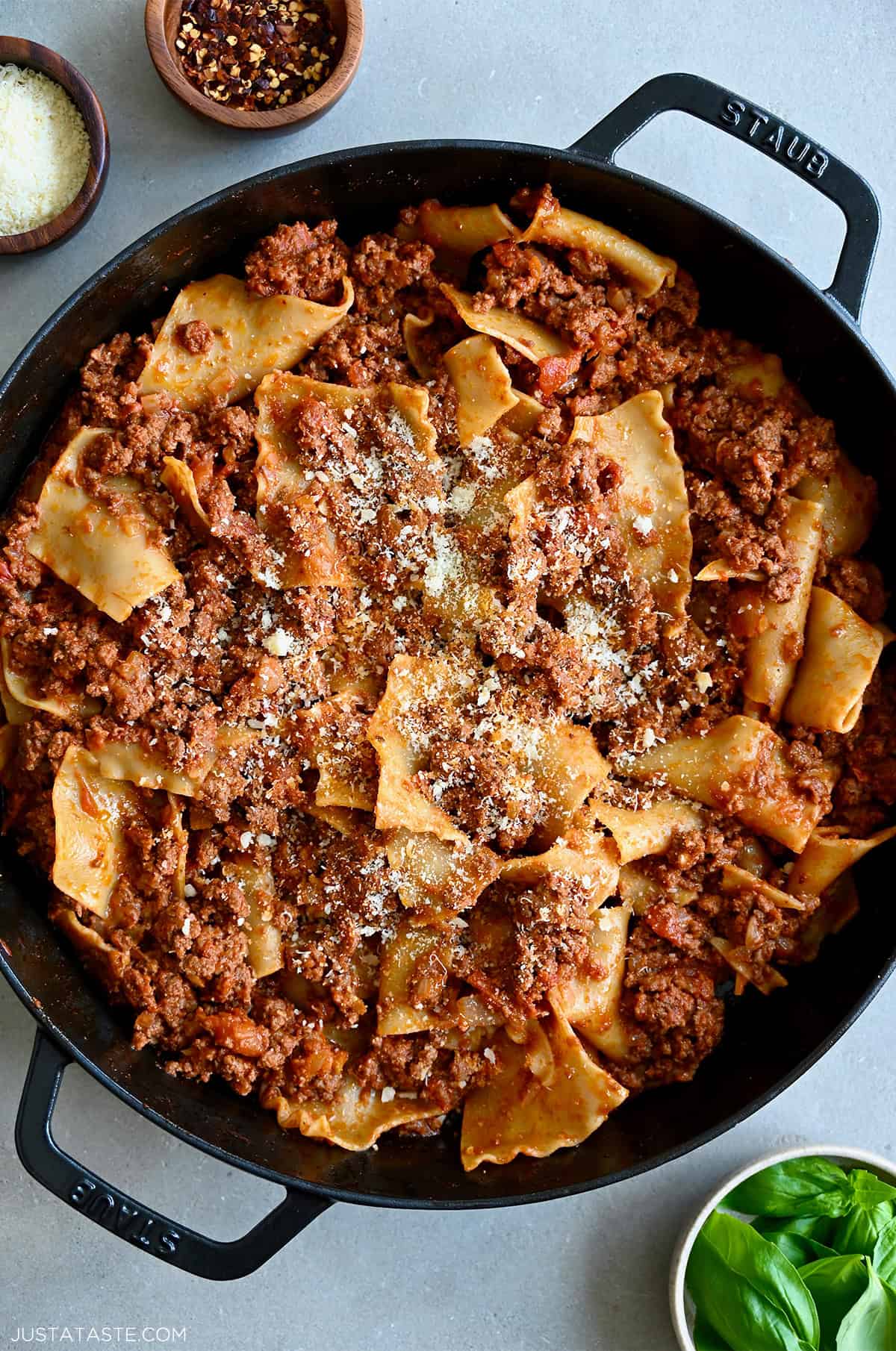 A cast iron skillet containing hearty beef lasagna garnished with grated Parmesan cheese.