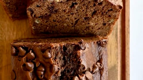 A loaf of double chocolate banana bread with chocolate chips on a bamboo cutting board.