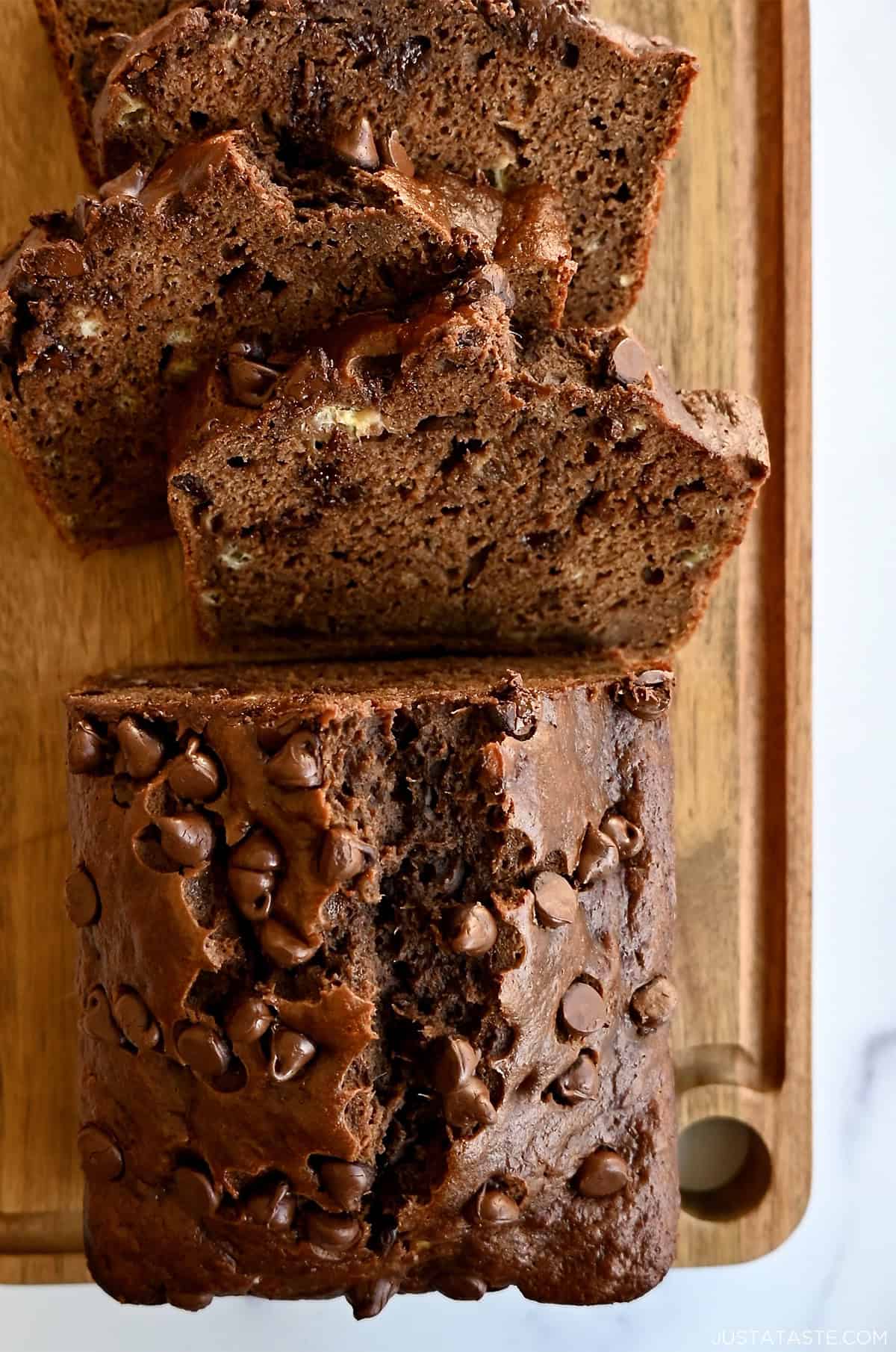 A loaf of double chocolate banana bread with chocolate chips on a bamboo cutting board.