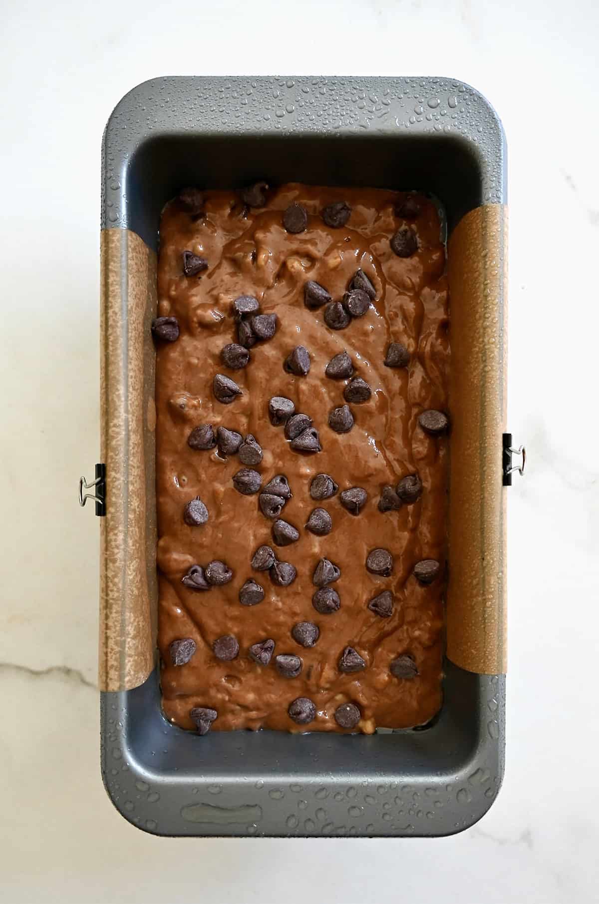 Unbaked chocolate banana bread topped with chocolate chips in a loaf pan lined with parchment paper.