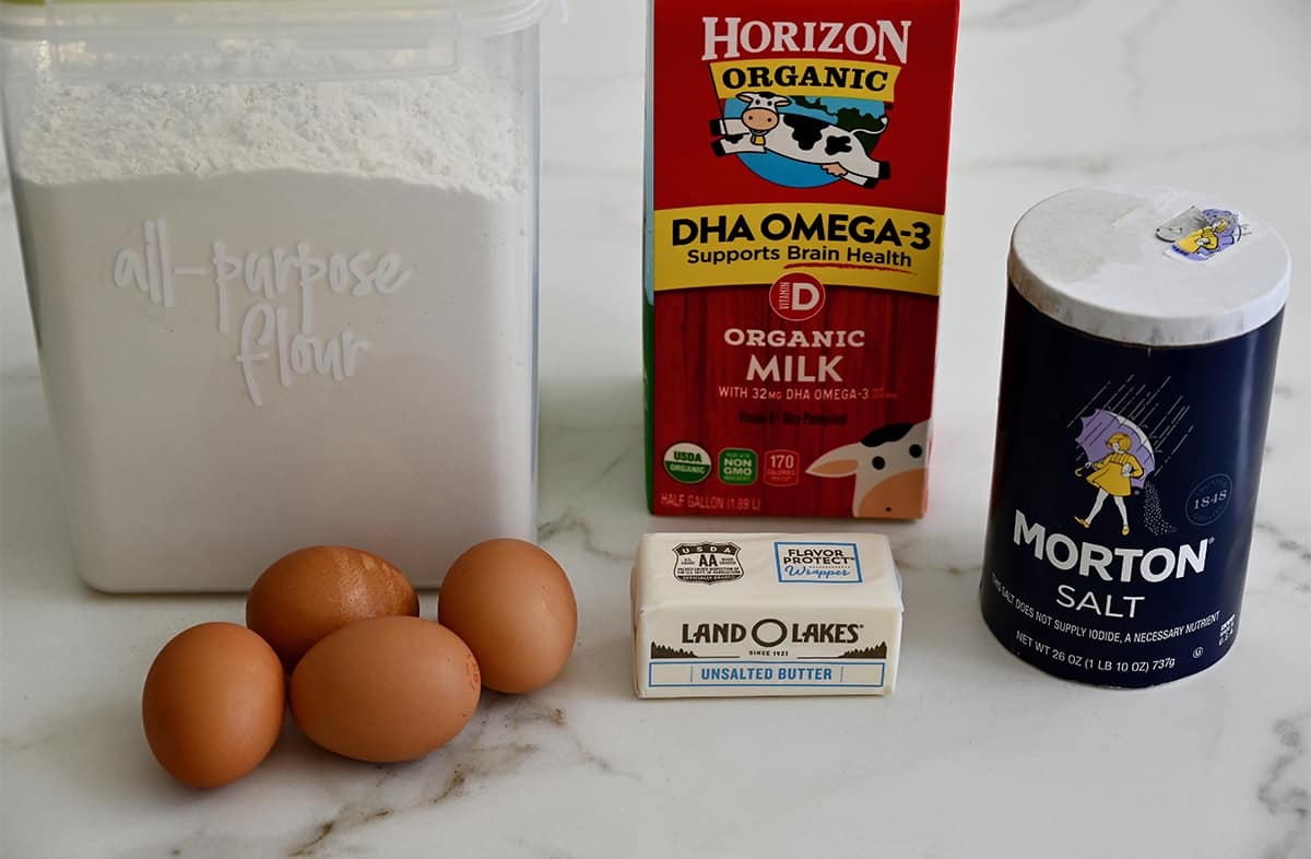 Flour in a clear container, four eggs, Horizon Organic whole milk, a stick of Land O' Lakes butter and Morton salt.