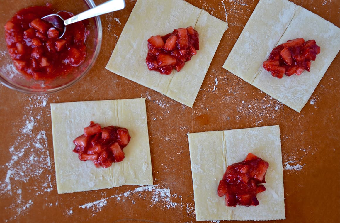 Strawberry rhubarb jam atop puff pastry squares on a wood cutting board