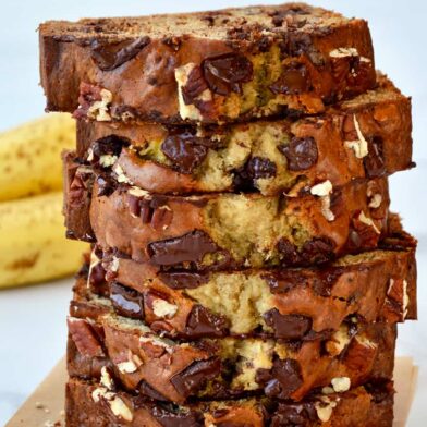 Slices of banana bread stacked on top of each other with bananas in the background
