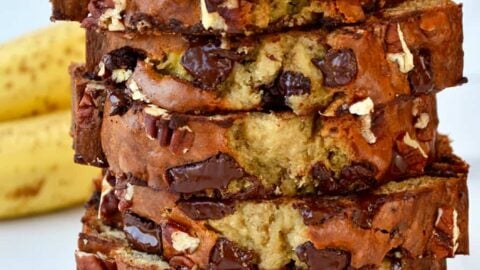 Slices of banana bread stacked on top of each other with bananas in the background