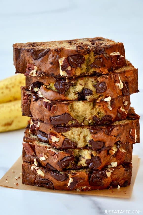 Slices of banana bread stacked on top of each other with bananas in the background