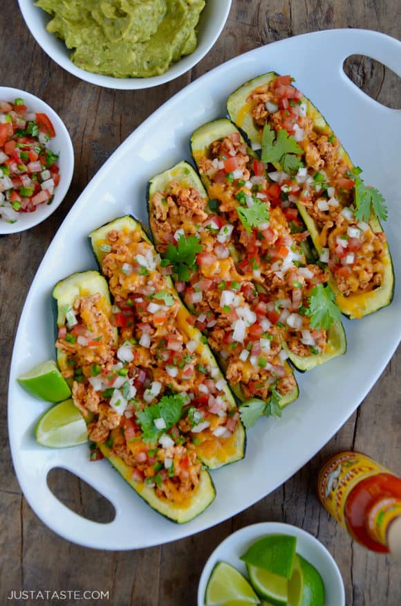 A white platter containing zucchini boats with small bowls of guacamole and salsa next to them