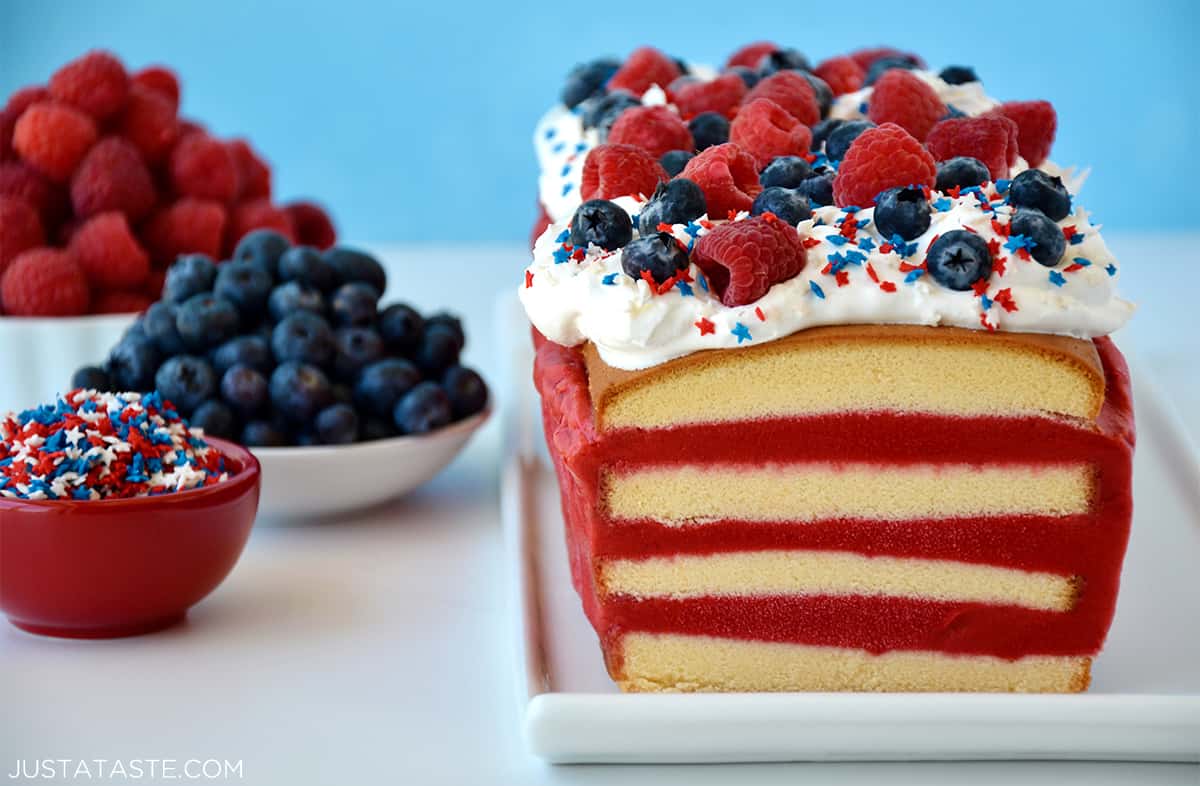 A 4th of July ice cream cake with layers of pound cake and raspberry sorbet topped with a thick layer of whipped cream, fresh berries, and red and blue star sprinkles. 