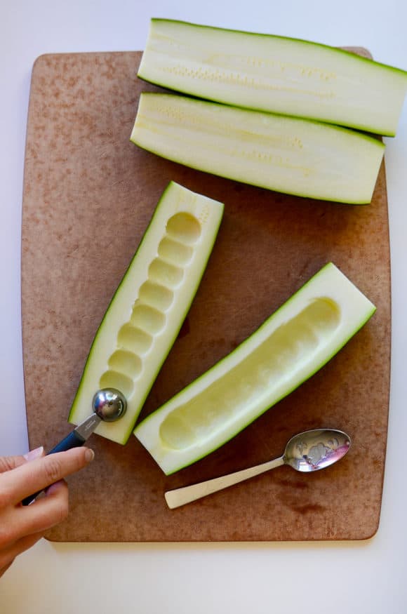 A cutting board containing halved zucchini with a melon baller