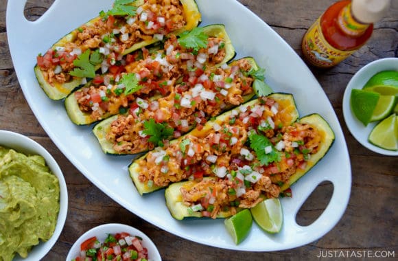 A white plate of zucchini boats surrounded by toppings and hot sauce