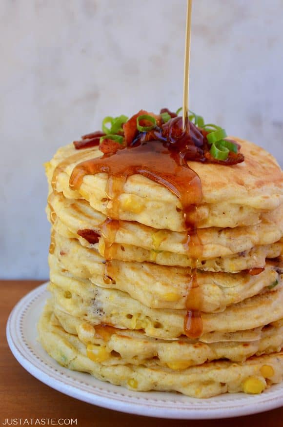 Tall stack of Sweet Corn Pancakes with Bacon topped with sliced scallions and drizzled with maple syrup