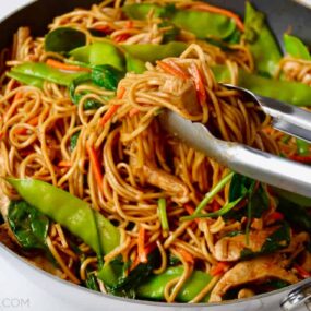 A skillet containing Chicken Lo Mein and tongs