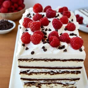 Ice cream sandwich cake with layers of whipped cream and topped with fresh raspberries and mini chocolate chips.