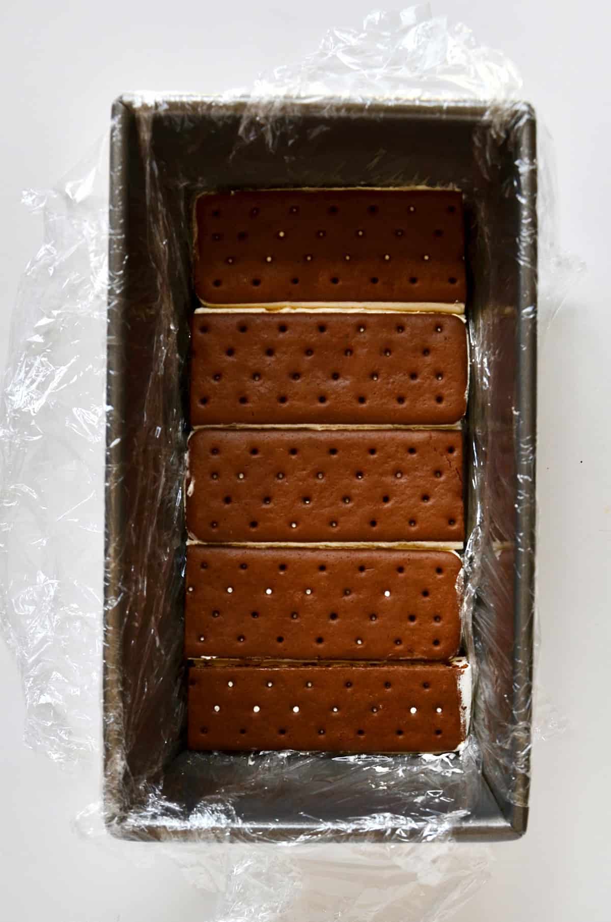 Ice cream sandwiches lining the bottom of a loaf pan lined with plastic wrap.