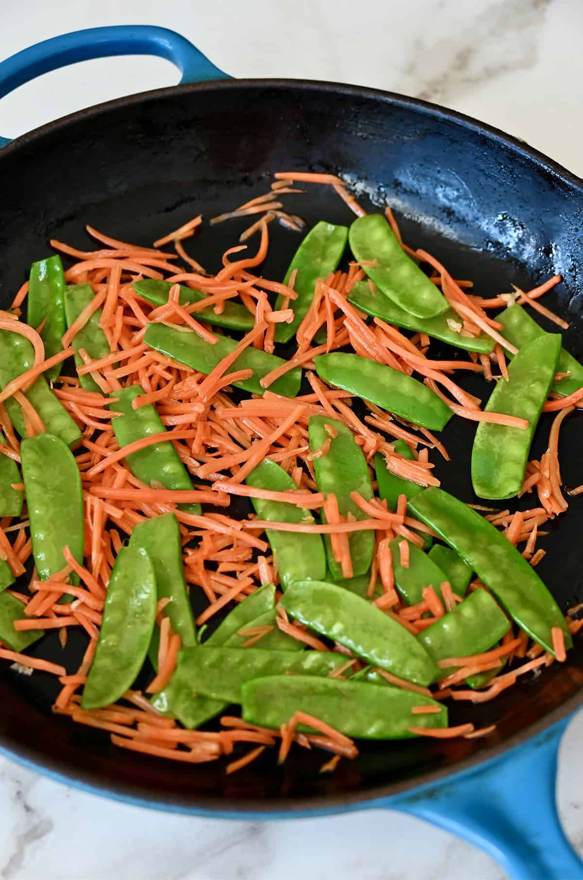 Stir-fried snow peas and carrots in a large skillet.