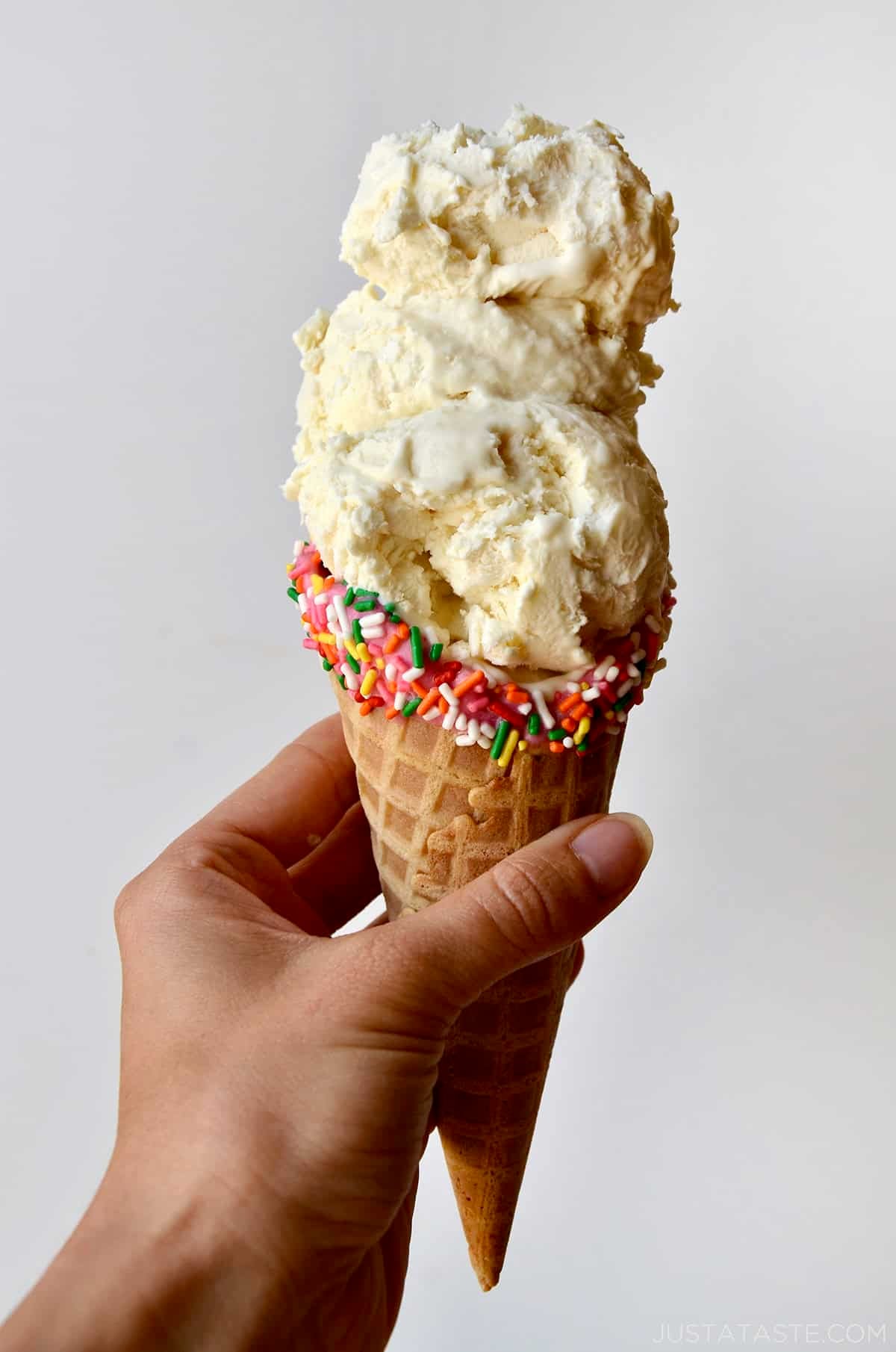 A hand holding a waffle cone with three scoops of no-churn vanilla ice cream.