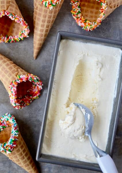 Creamy no-churn ice cream in a loaf pan with an ice cream scoop next to waffle cones.