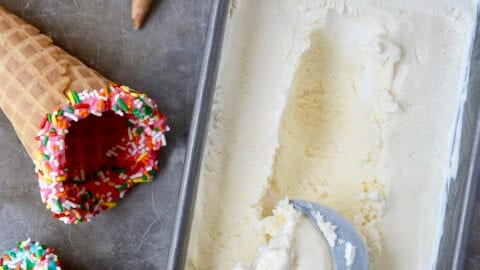 Creamy no-churn ice cream in a loaf pan with an ice cream scoop next to waffle cones.