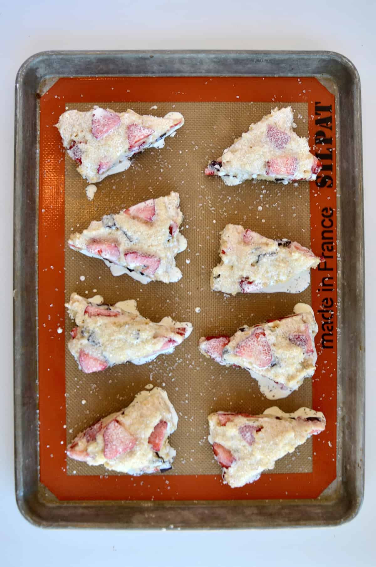 Unbaked strawberry scones brushed with heavy cream on a Silpat-lined baking sheet.