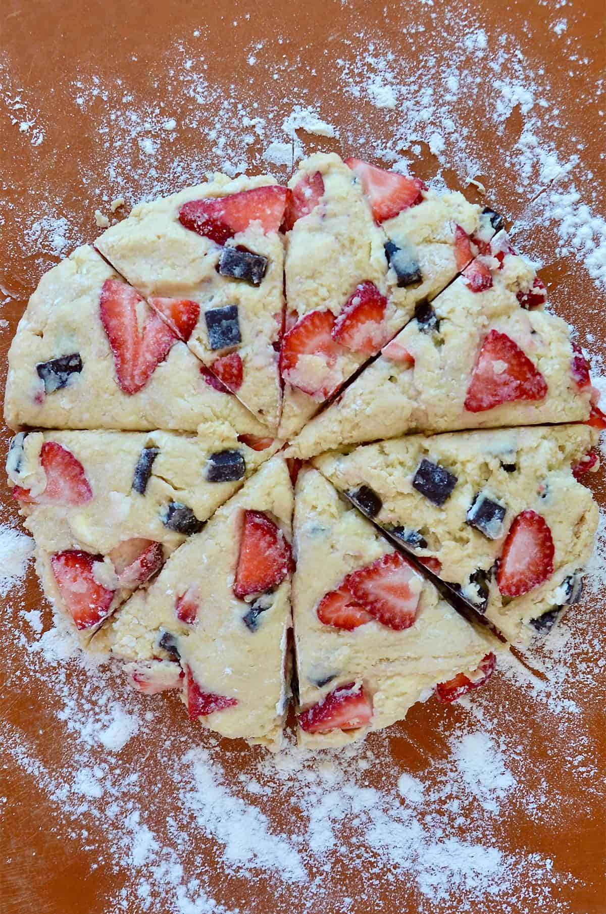 Unbaked strawberry chocolate chunk scones cut into eight wedges on a floured work surface.