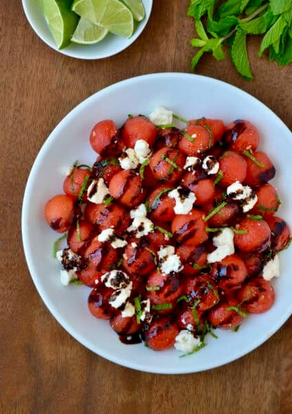 Watermelon salad with balsamic syrup, crumbled feta cheese and fresh mint in a white serving bowl.
