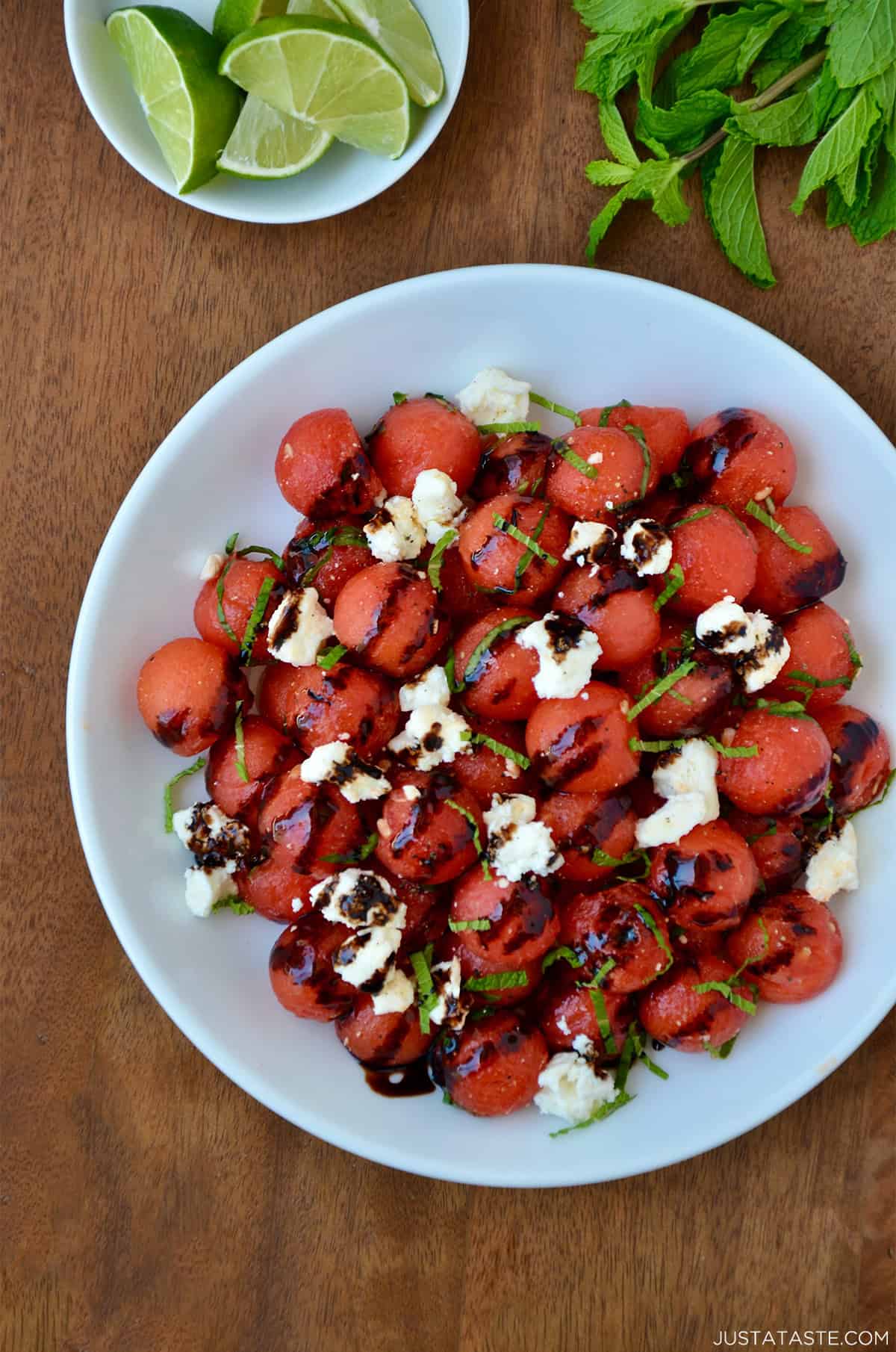 Watermelon salad with balsamic syrup, crumbled feta cheese and fresh mint in a white serving bowl.