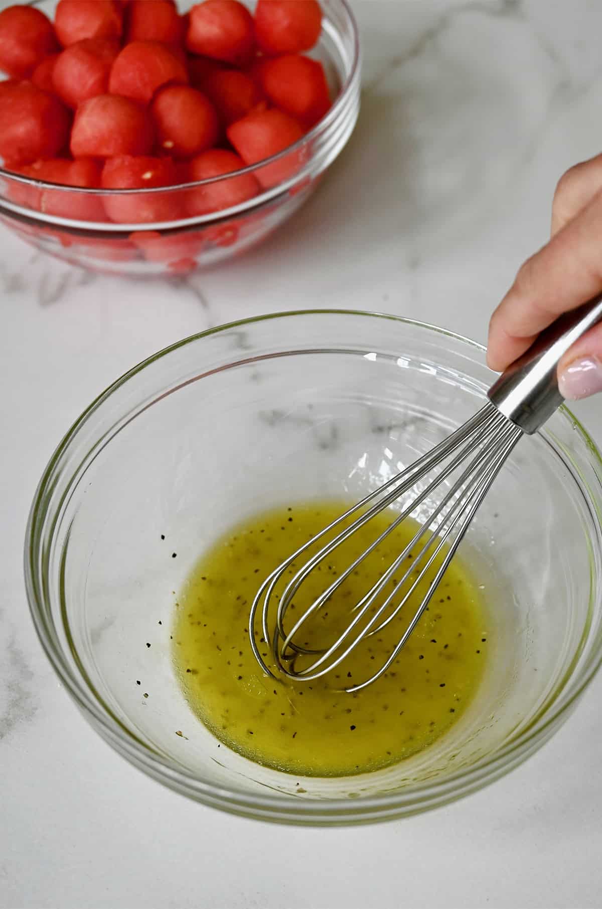 Olive oil, lime juice, salt and pepper being whisked together in a small bowl.