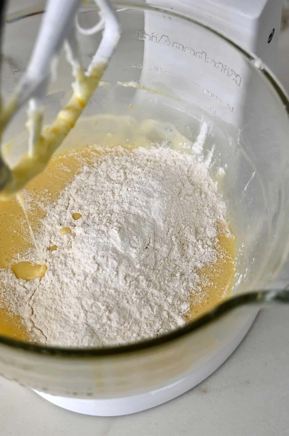 Adding flour to a stand mixer bowl to make cake batter.