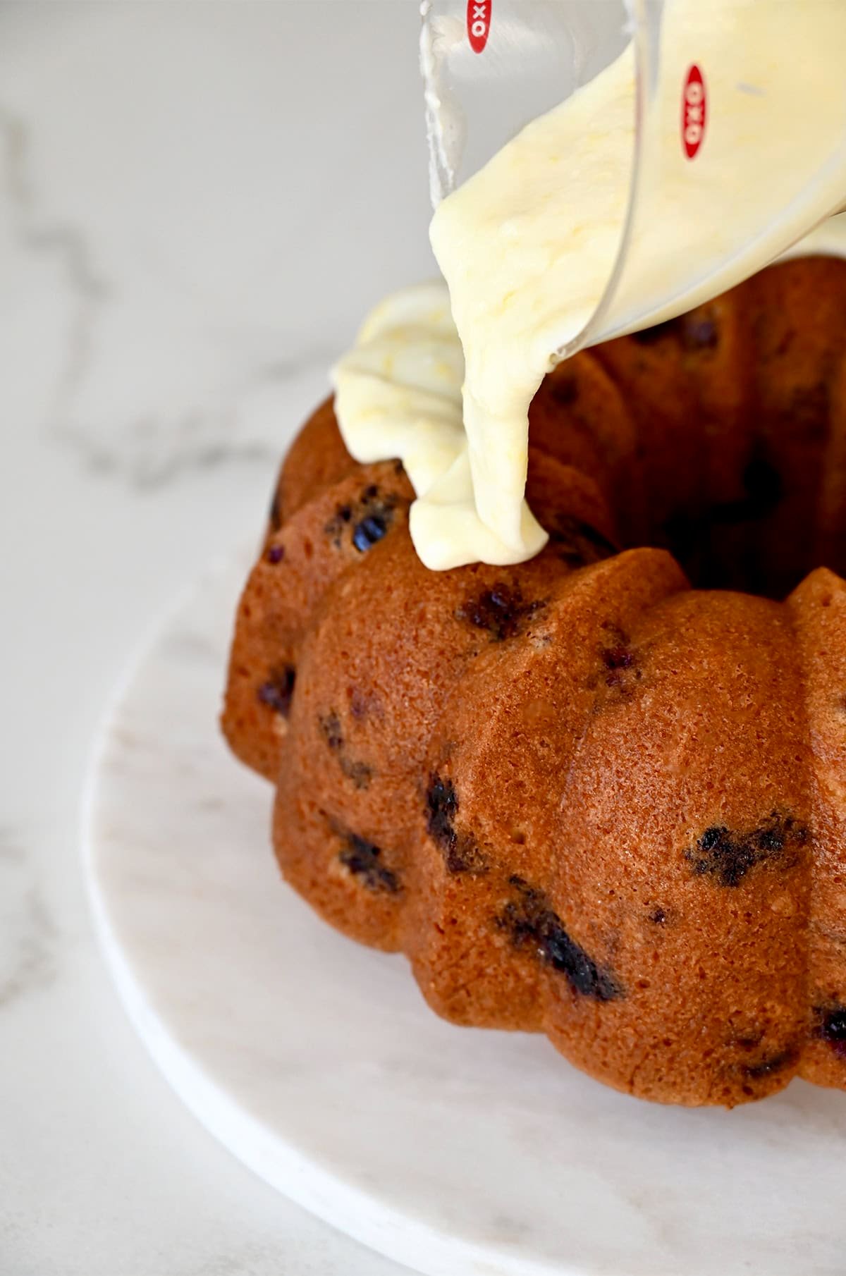 Adding a lemon glaze to a cooled blueberry pound cake.