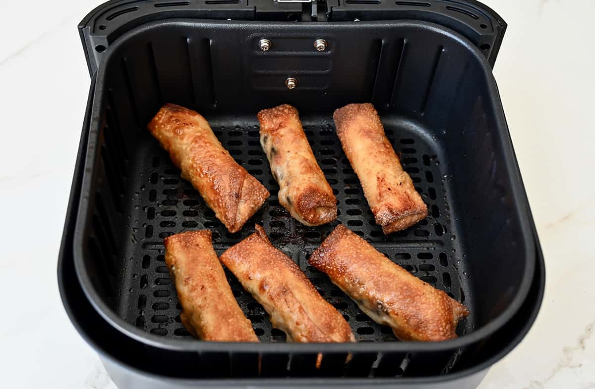 An air fryer basket containing egg rolls