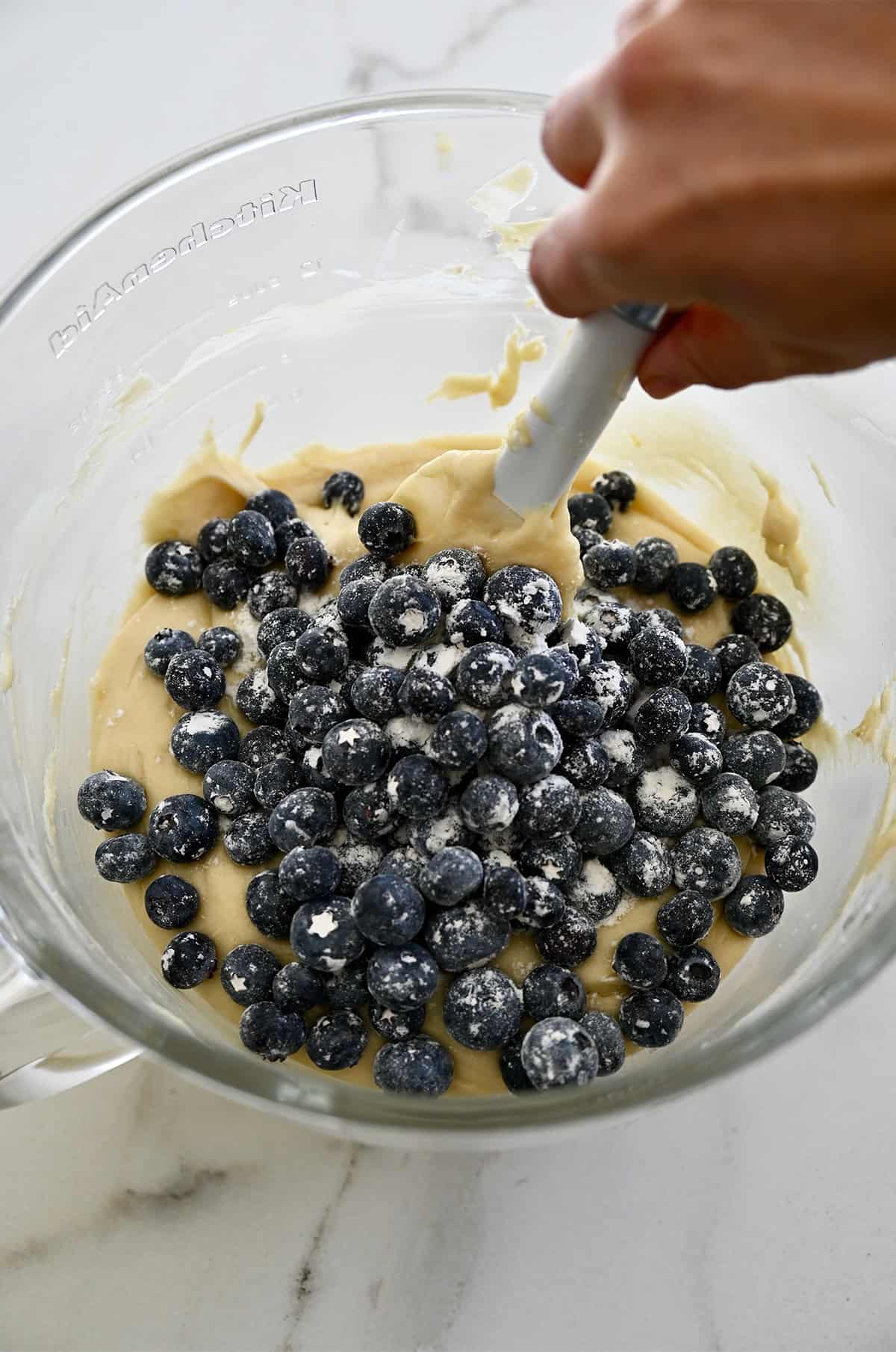 Folding flour-coated blueberries into cream cheese pound cake batter with a spatula.