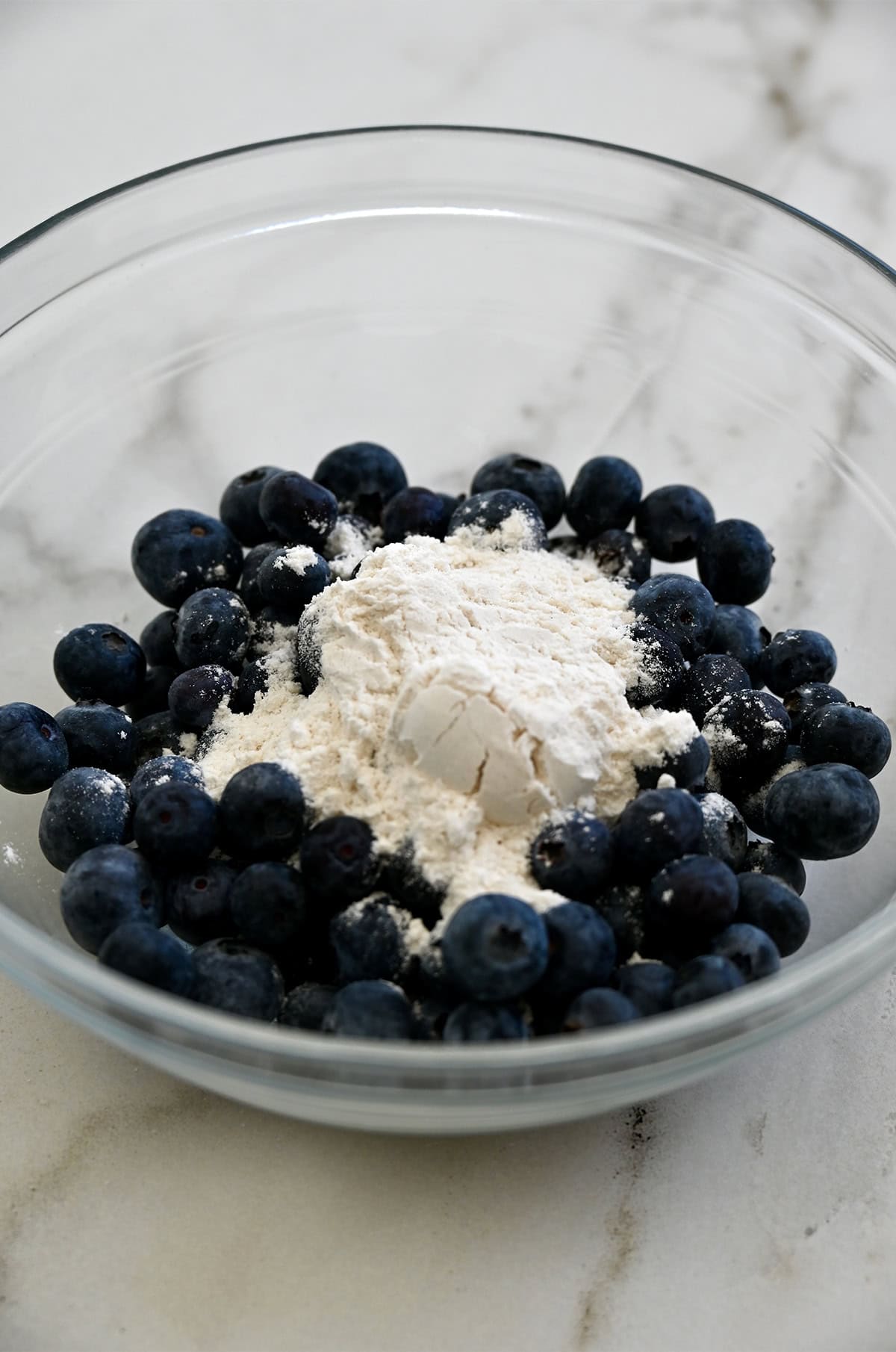 Tossing blueberries with flour in a small bowl.