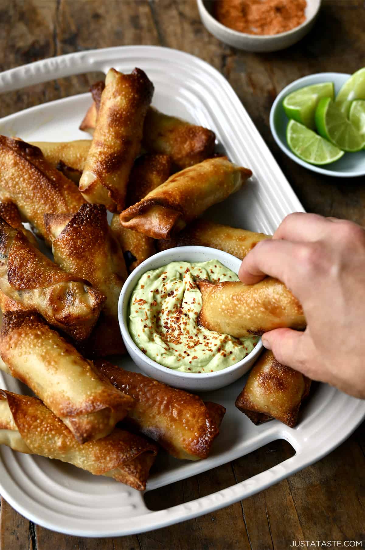 A hand dipping an egg roll into avocado dip topped with tajin