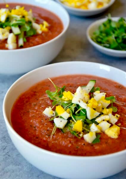 A bowl containing chilled gazpacho topped with microgreens, chopped hard-boiled egg and cucumber.