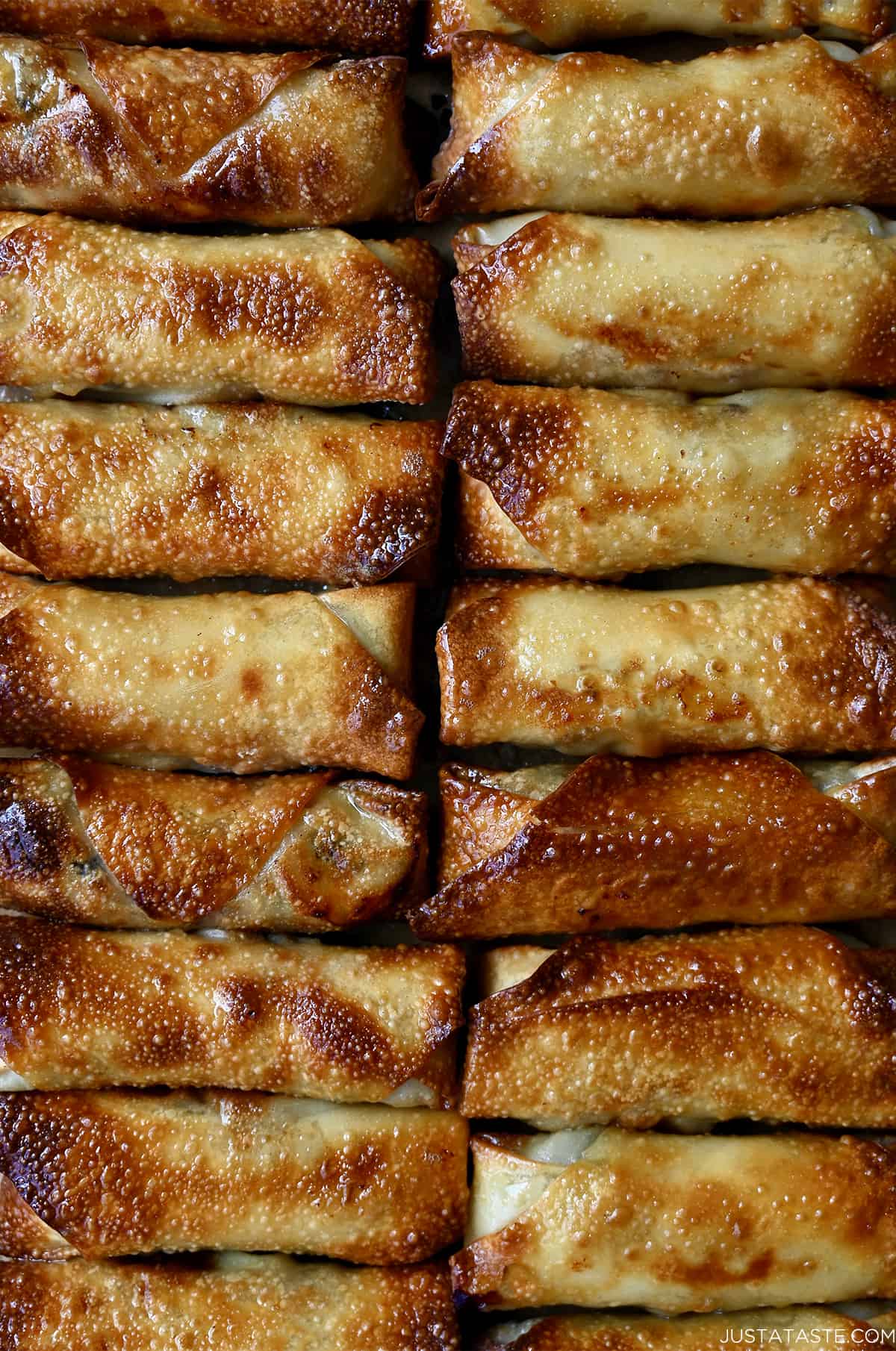 A close up view of air-fried spring rolls lined up on a baking sheet