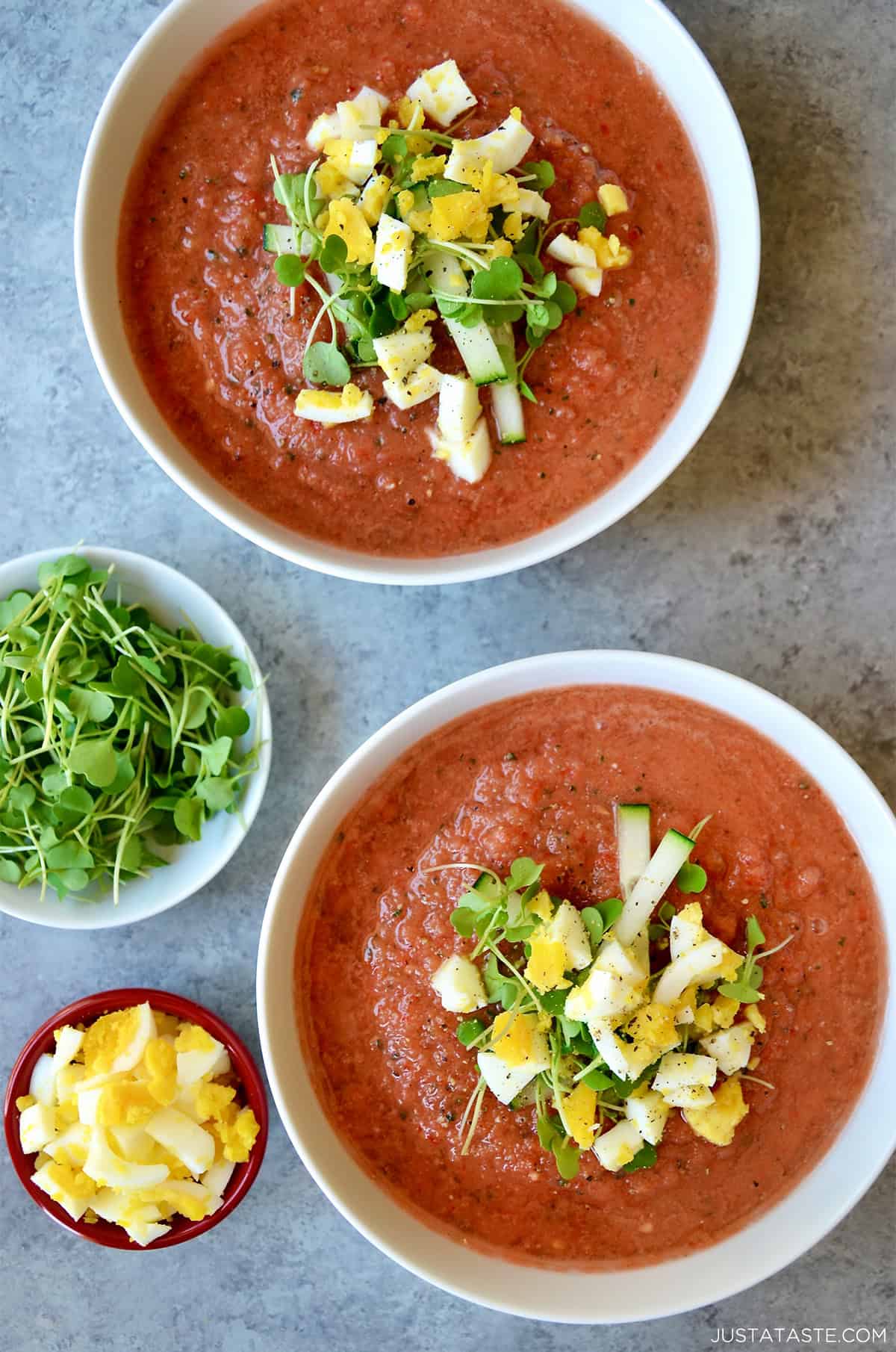 Two bowls containing gazpacho topped with chopped hard-boiled egg, microgreens, and cucumber slices.