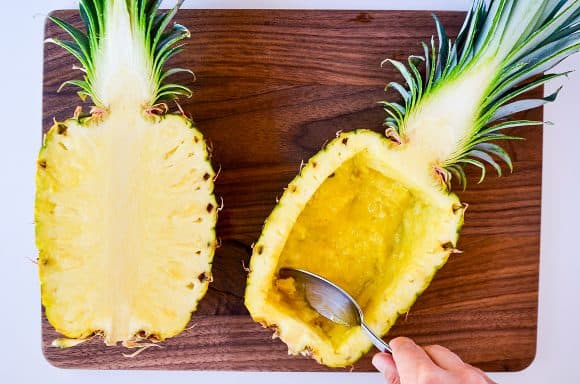 Halved pineapples being hollowed out with a spoon