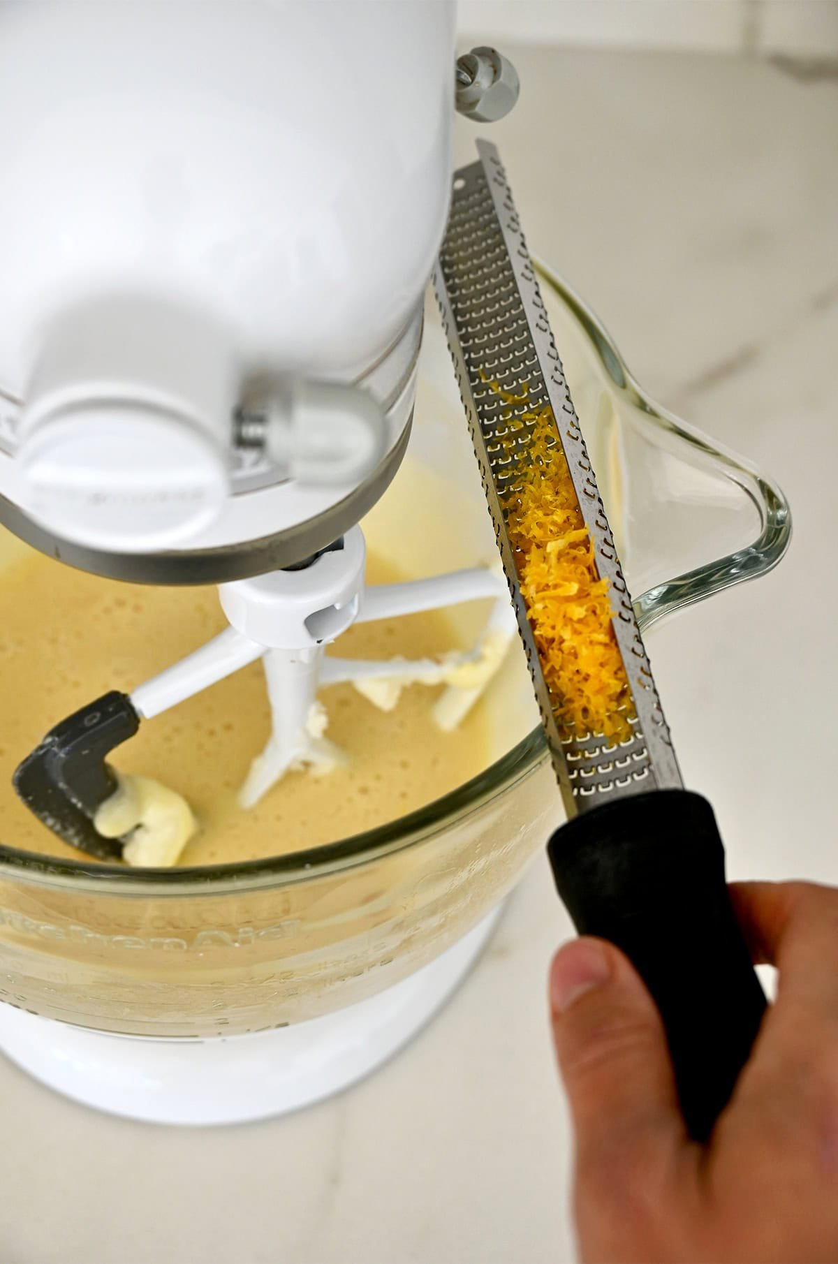 A microplane with lemon zest over a bowl containing pound cake batter.