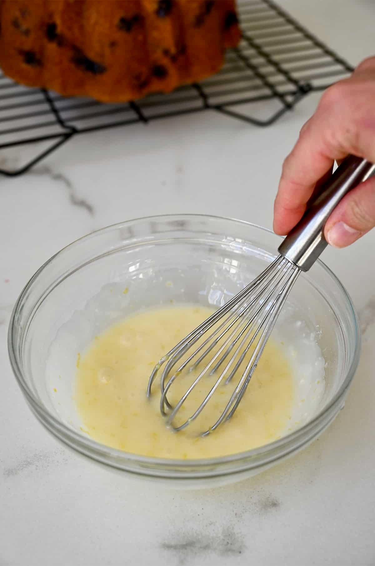 Whisking together lemon juice, lemon zest and powdered sugar in a bowl to make a glaze. 