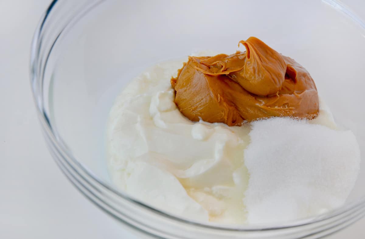 A clear bowl containing yogurt, peanut butter and sugar.