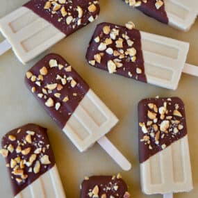 A top-down view of peanut butter frozen yogurt pops that have been dipped in chocolate and sprinkled with chopped peanuts.
