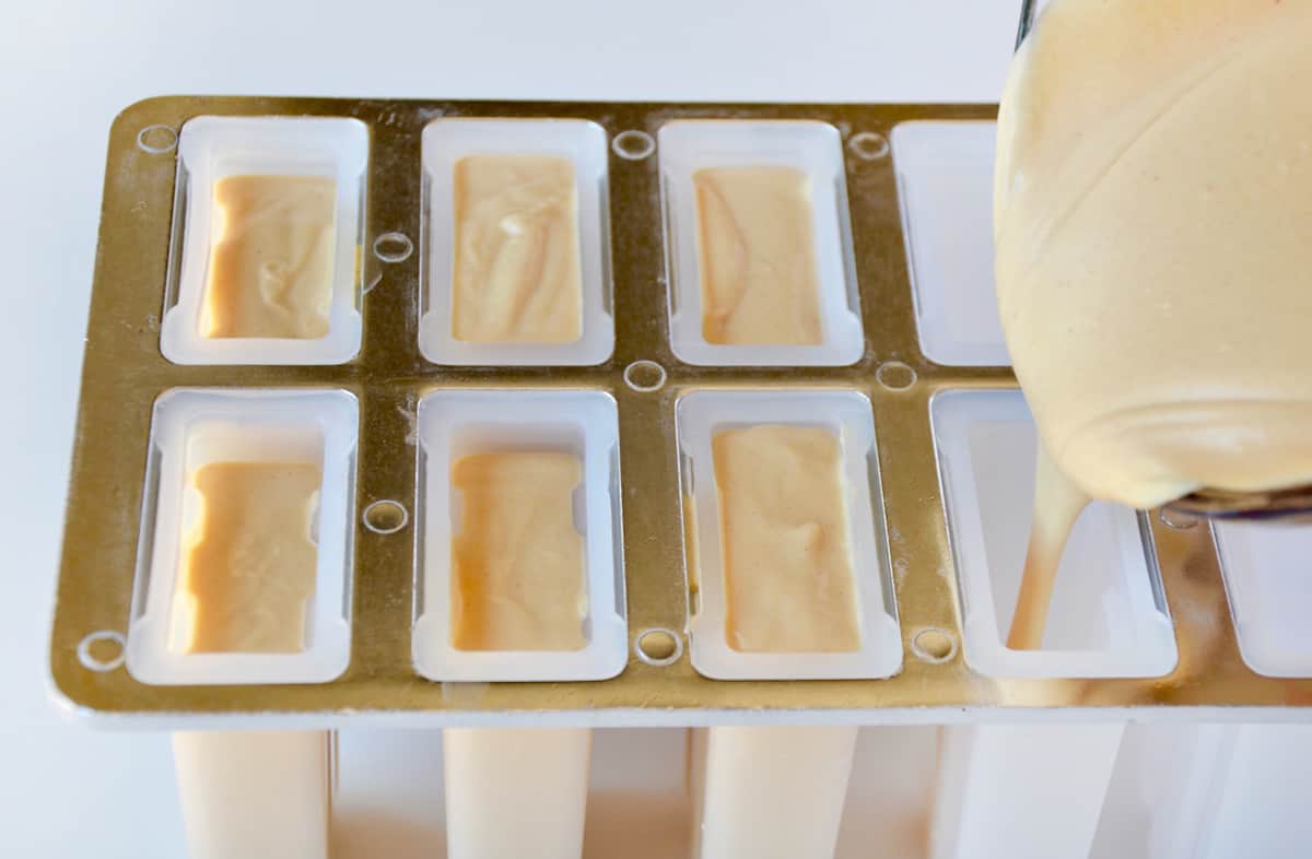 A popsicle mold being filled with a peanut butter-yogurt mixture. 