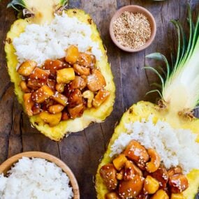Two pineapple bowls filled with chicken and white rice