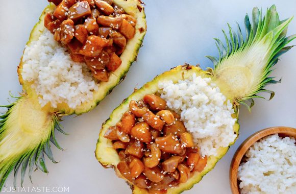 A hollowed out halved pineapple containing white rice and Sticky Pineapple Chicken