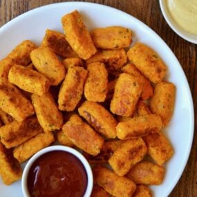 Baked butternut squash tots on a white plate with ketchup and mustard