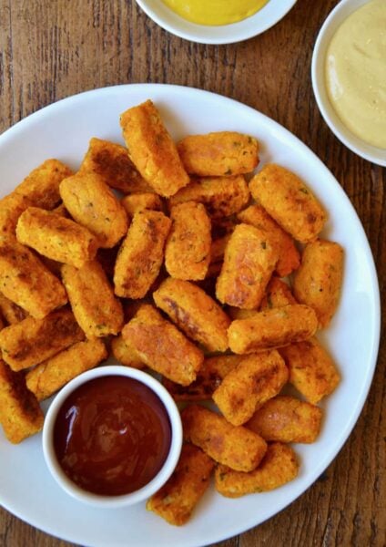 Baked butternut squash tots on a white plate with ketchup and mustard