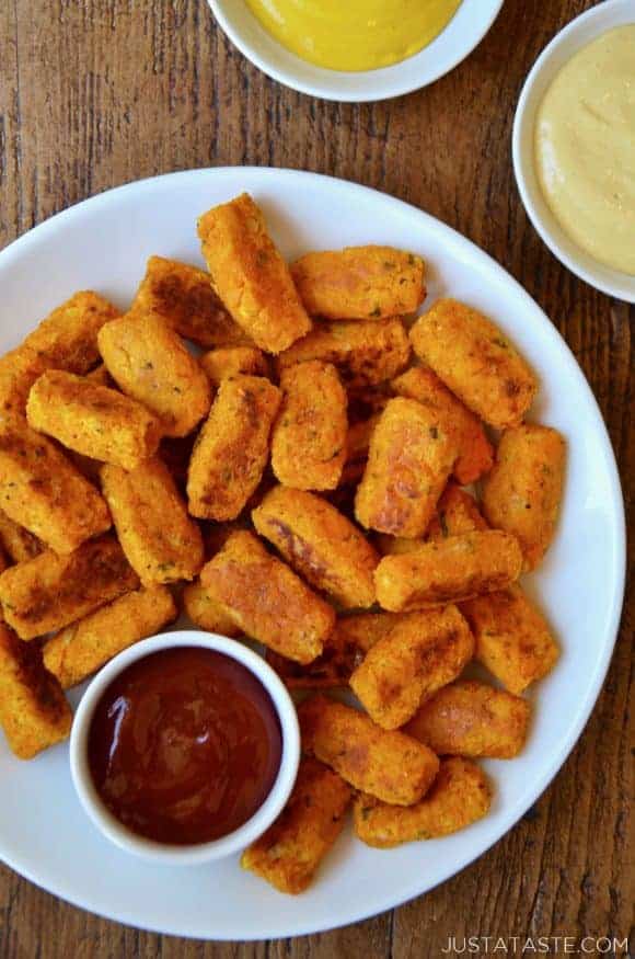 Baked butternut squash tots on a white plate with ketchup and mustard