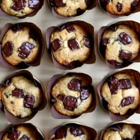 Golden brown banana chocolate chip muffins in cupcake liners in a muffin tin.