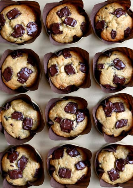 Golden brown banana chocolate chip muffins in cupcake liners in a muffin tin.